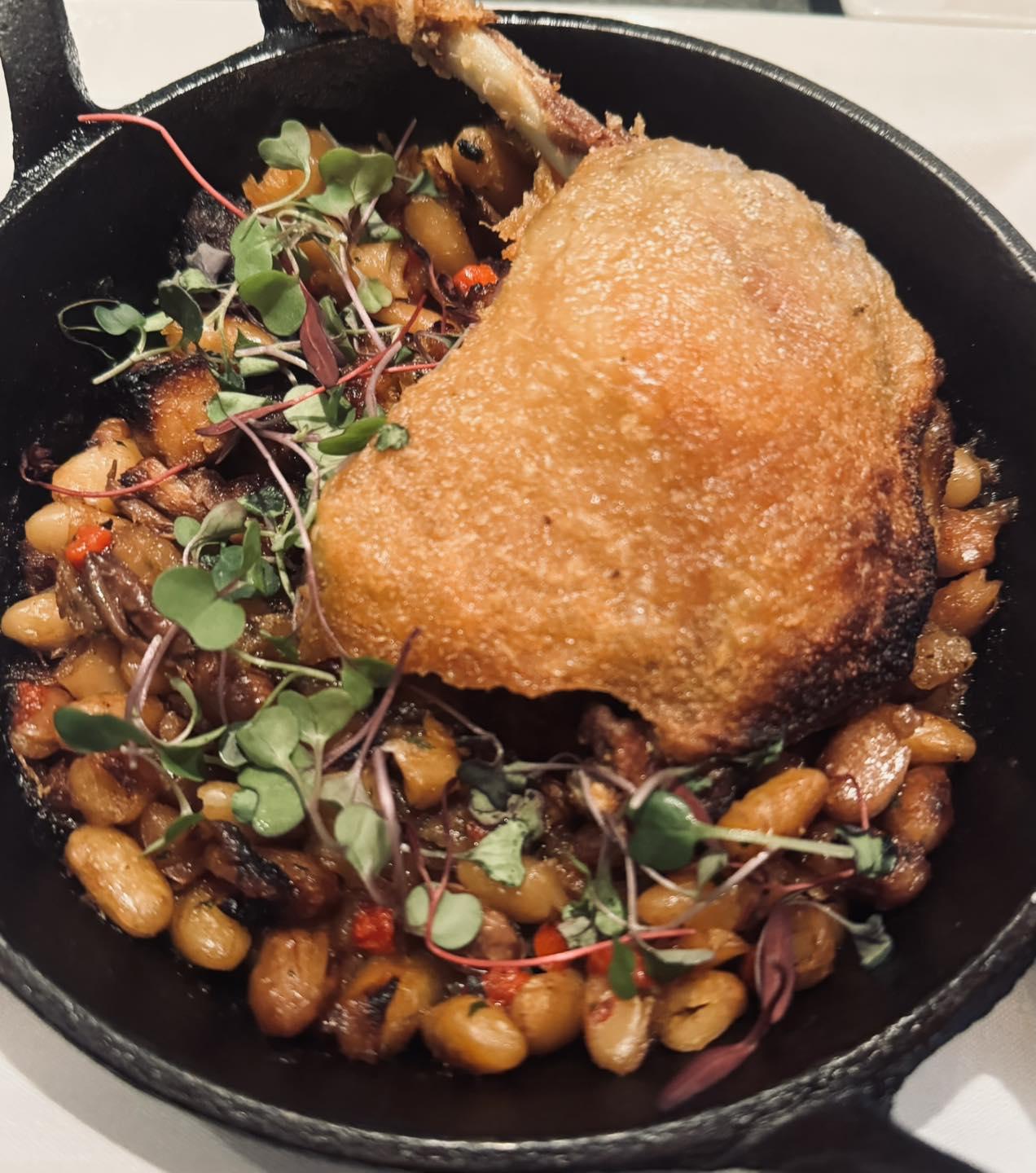 Crispy duck leg on beans and greens in a skillet.