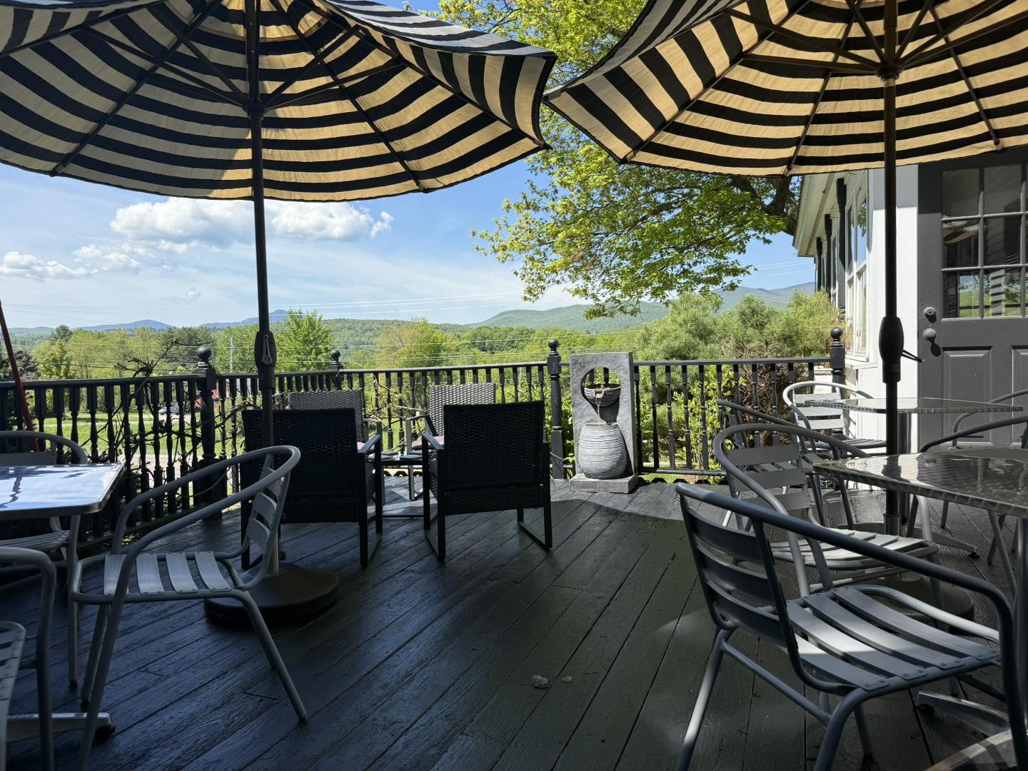 Shaded patio with striped umbrellas, overlooking green landscape.