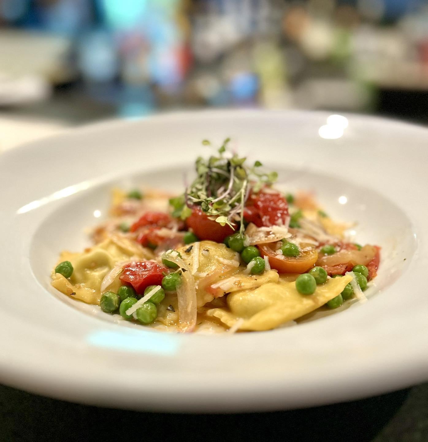 Ravioli with tomatoes, peas, and sprouts on a white plate.