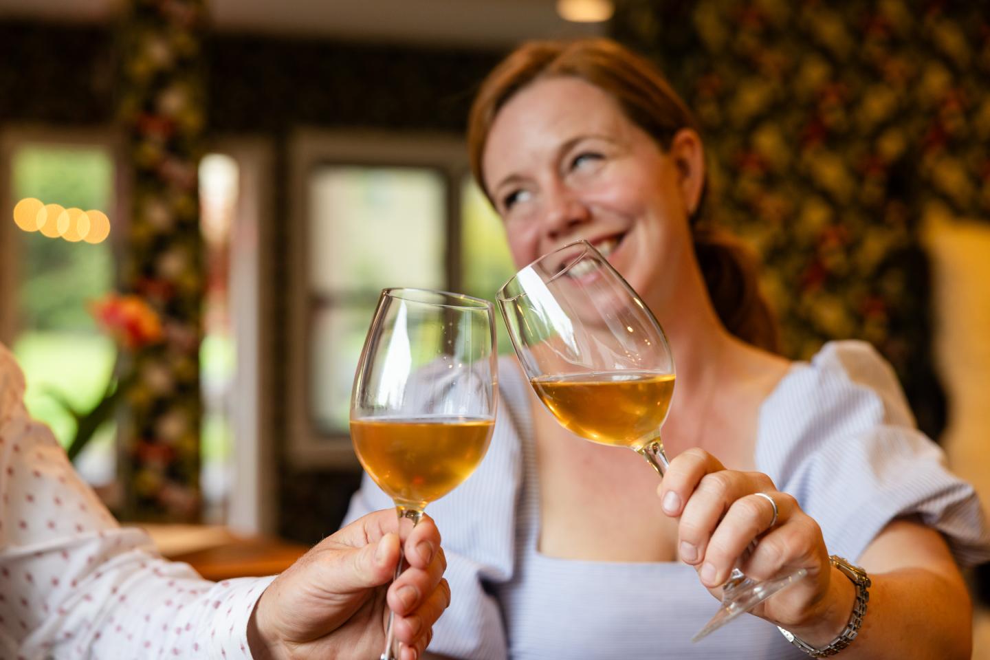 Smiling woman toasting with wine glasses indoors.