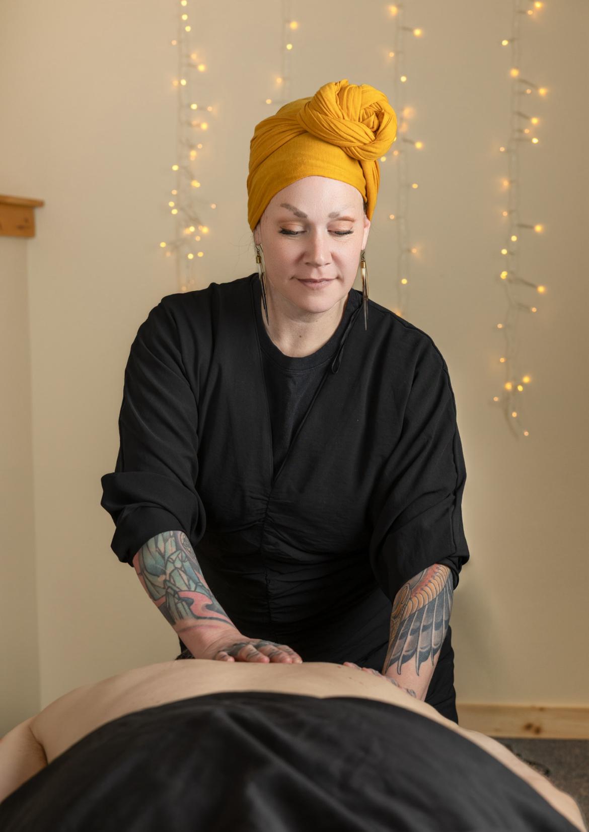 Massage therapist wearing a yellow headscarf, focused on a back massage.