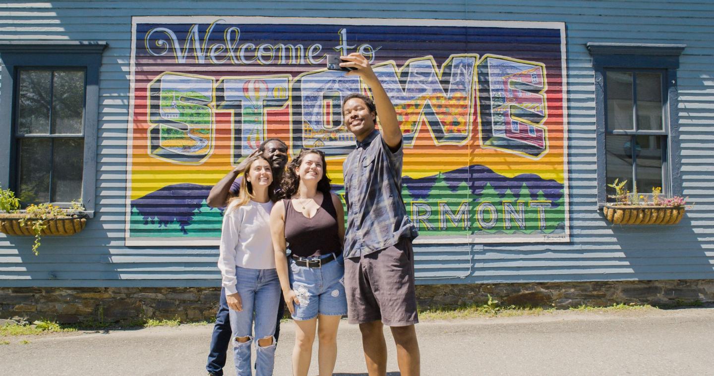 Four people smiling and taking a selfie in front of a colorful mural.