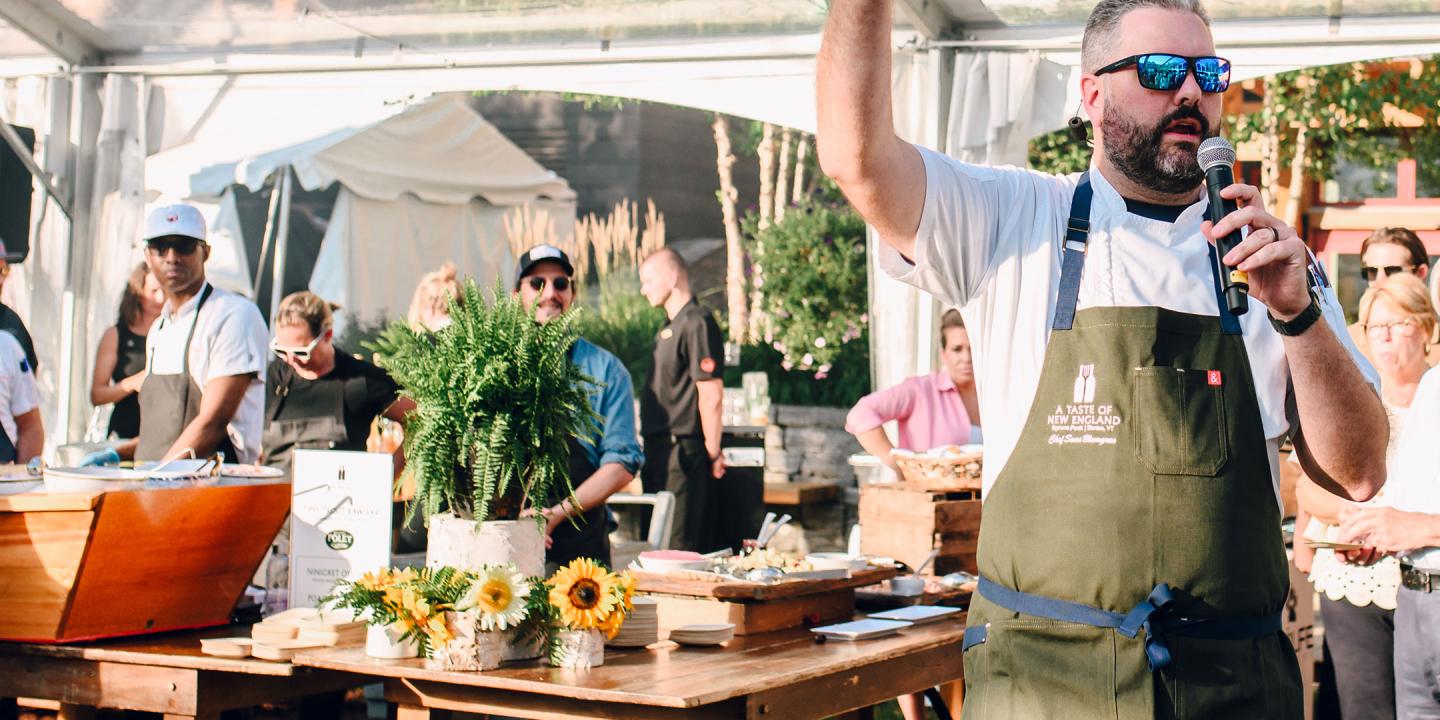 Man speaking at an outdoor food event, holding a microphone.