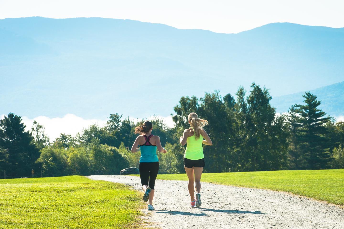 Two women jogging on a path with mountains in the background.