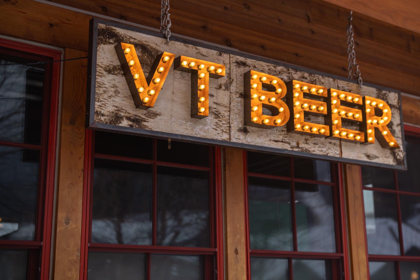 Rustic sign with lit letters "VT BEER" hanging above a window