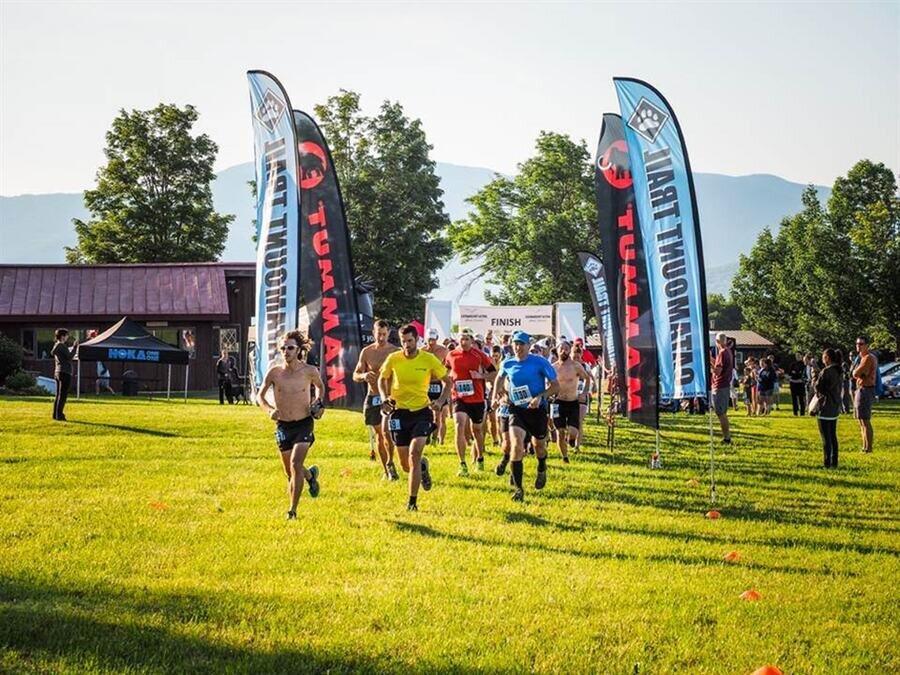 Runners starting a race on a grassy field with blue banners and trees in the background.