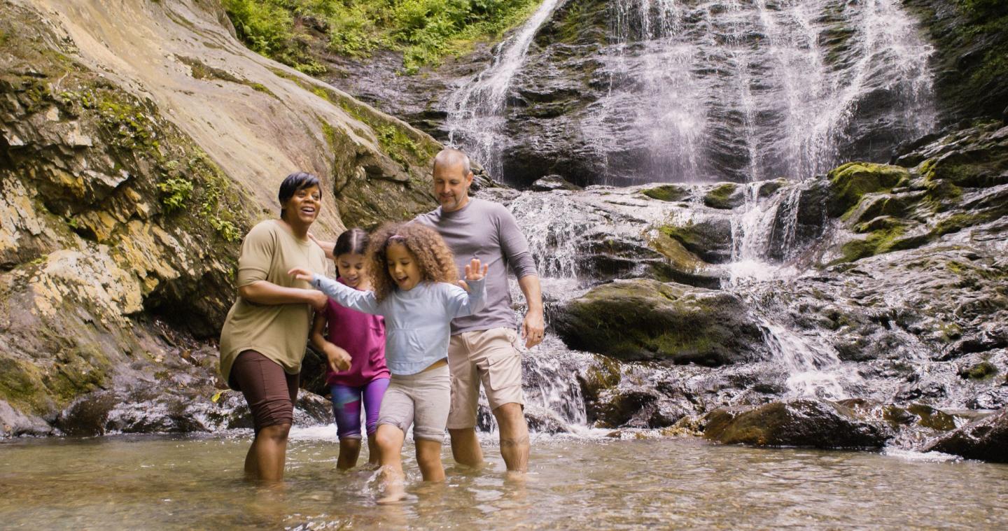 Family smiling by a waterfall, standing in a rocky stream.