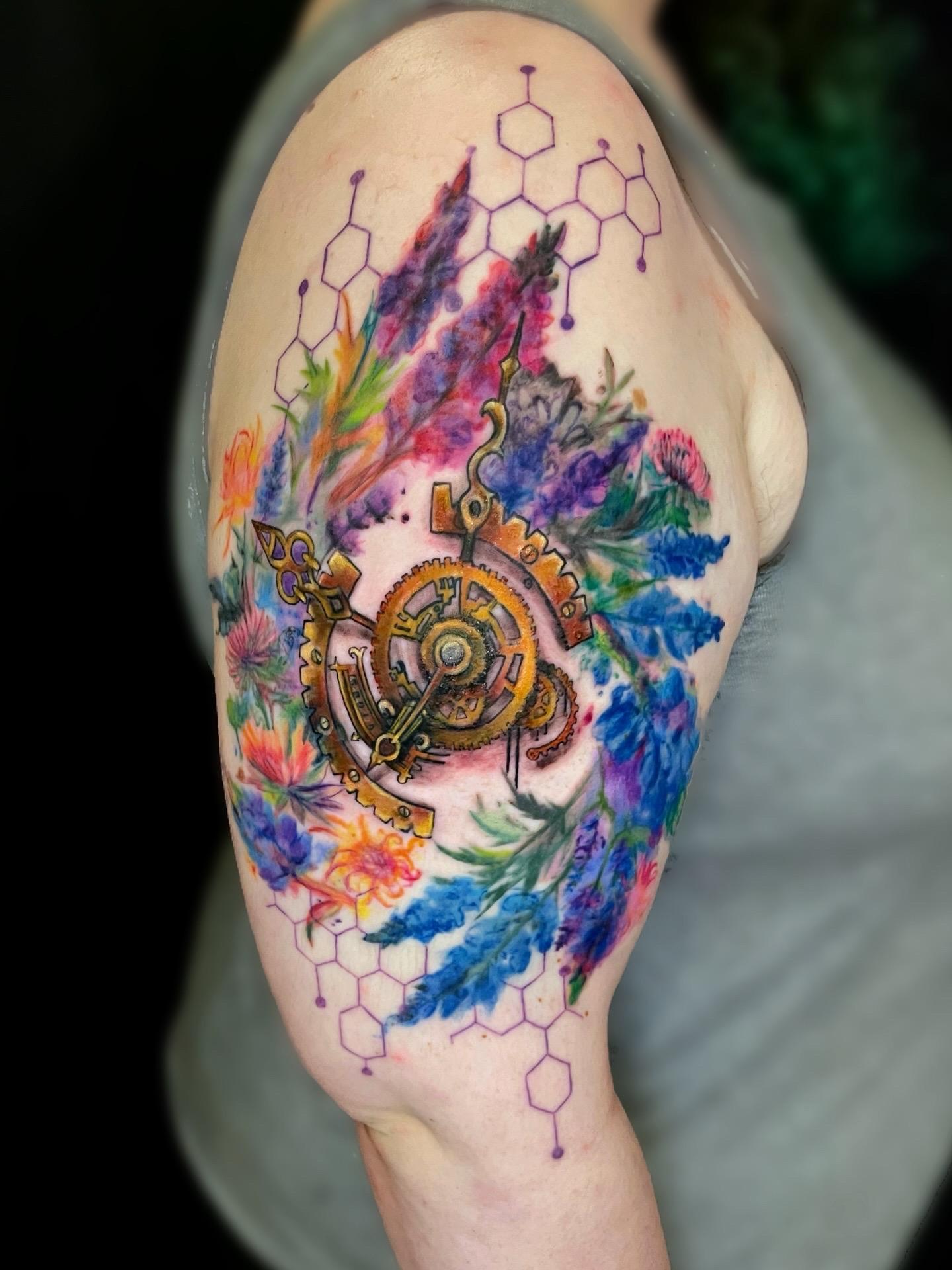 Colorful tattoo on upper arm with feathers and chemical structures.