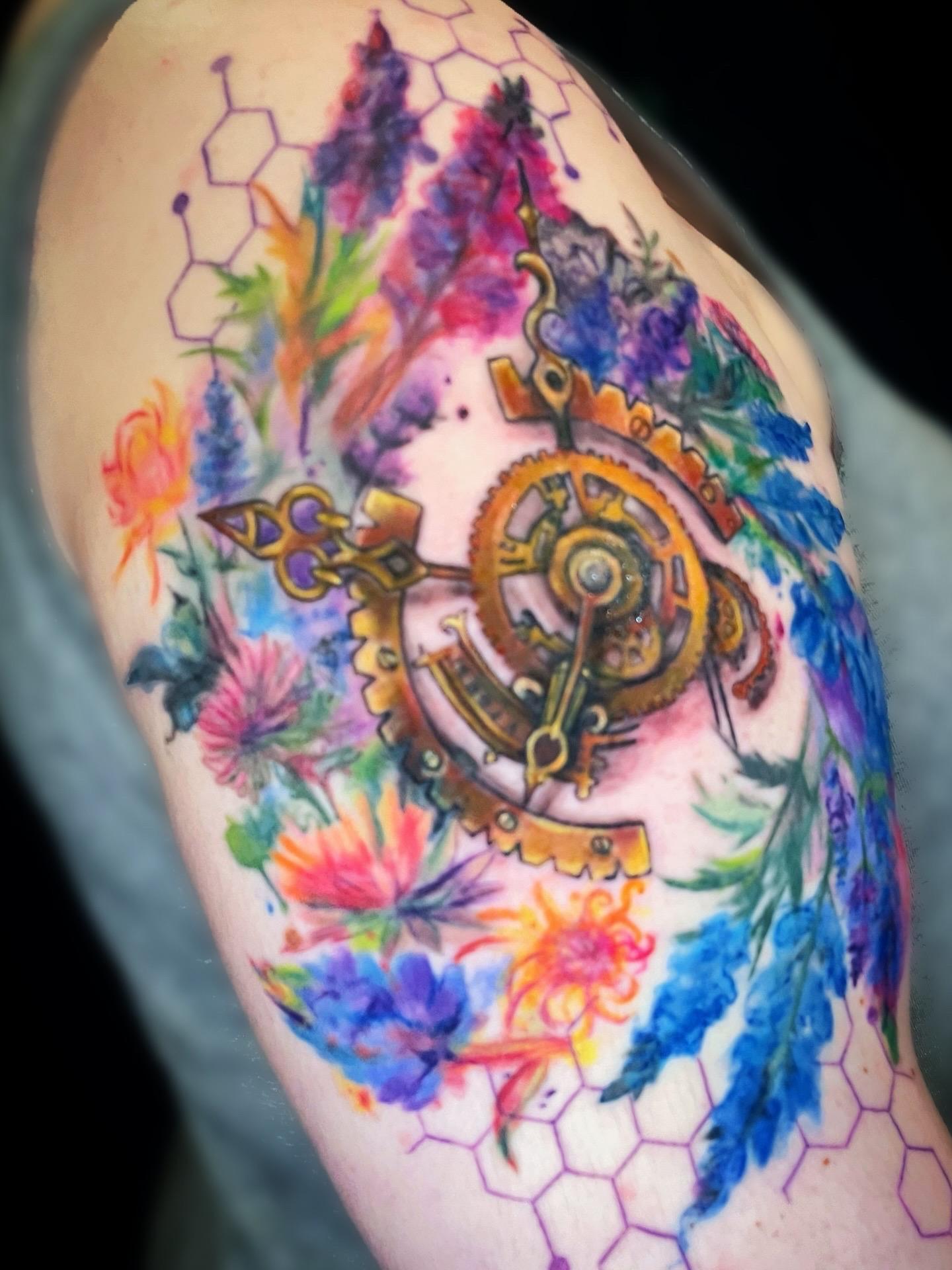 Colorful tattoo with flowers and geometric patterns on an upper arm.