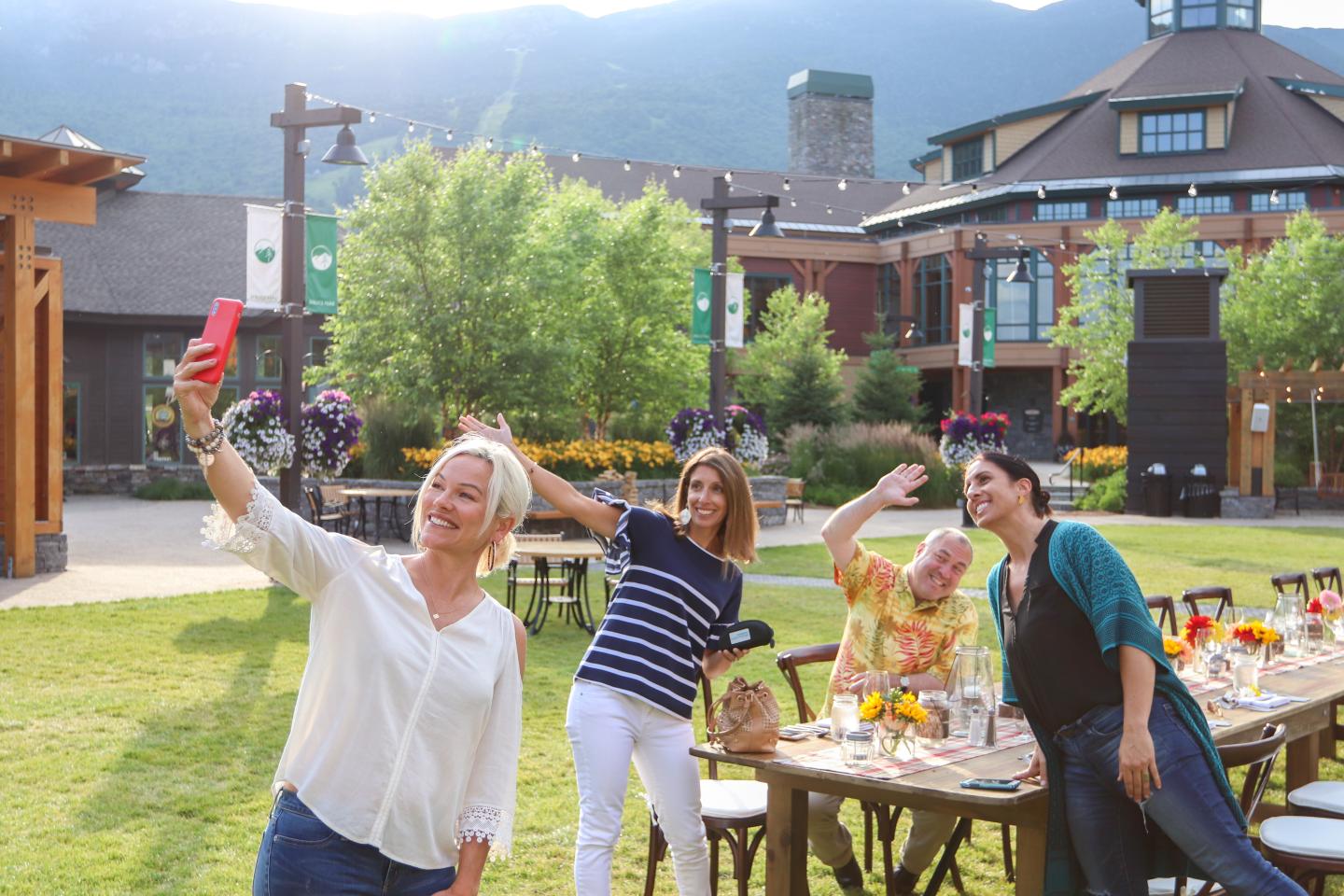 Four people happily taking a selfie outdoors near a table set up in a courtyard.