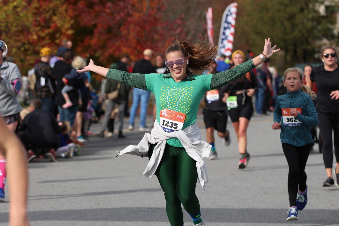 Runner in green celebrates during a race on an autumn day.