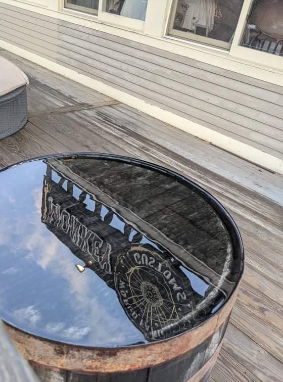 Water barrel reflecting a roof and sky on a wooden deck.