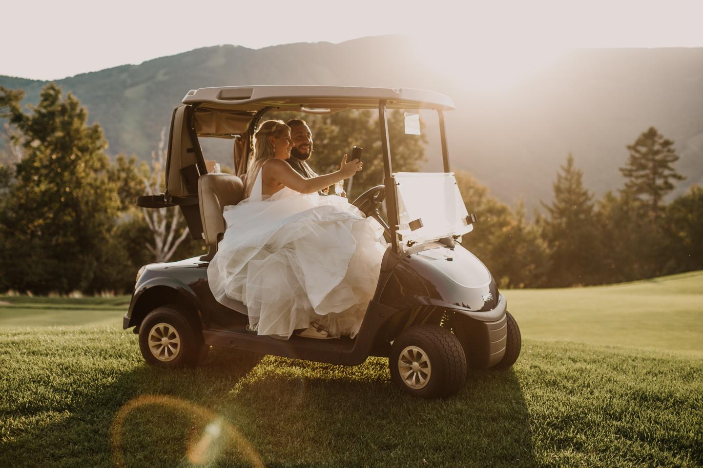 Bride in a golf cart on a sunny course with mountains in the background.