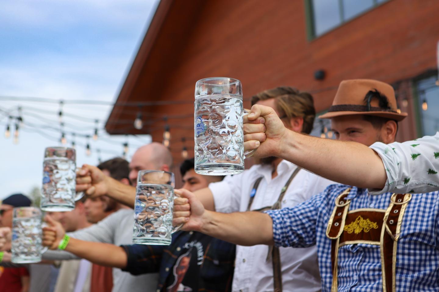 People in traditional attire holding large beer mugs at an outdoor Oktoberfest event.