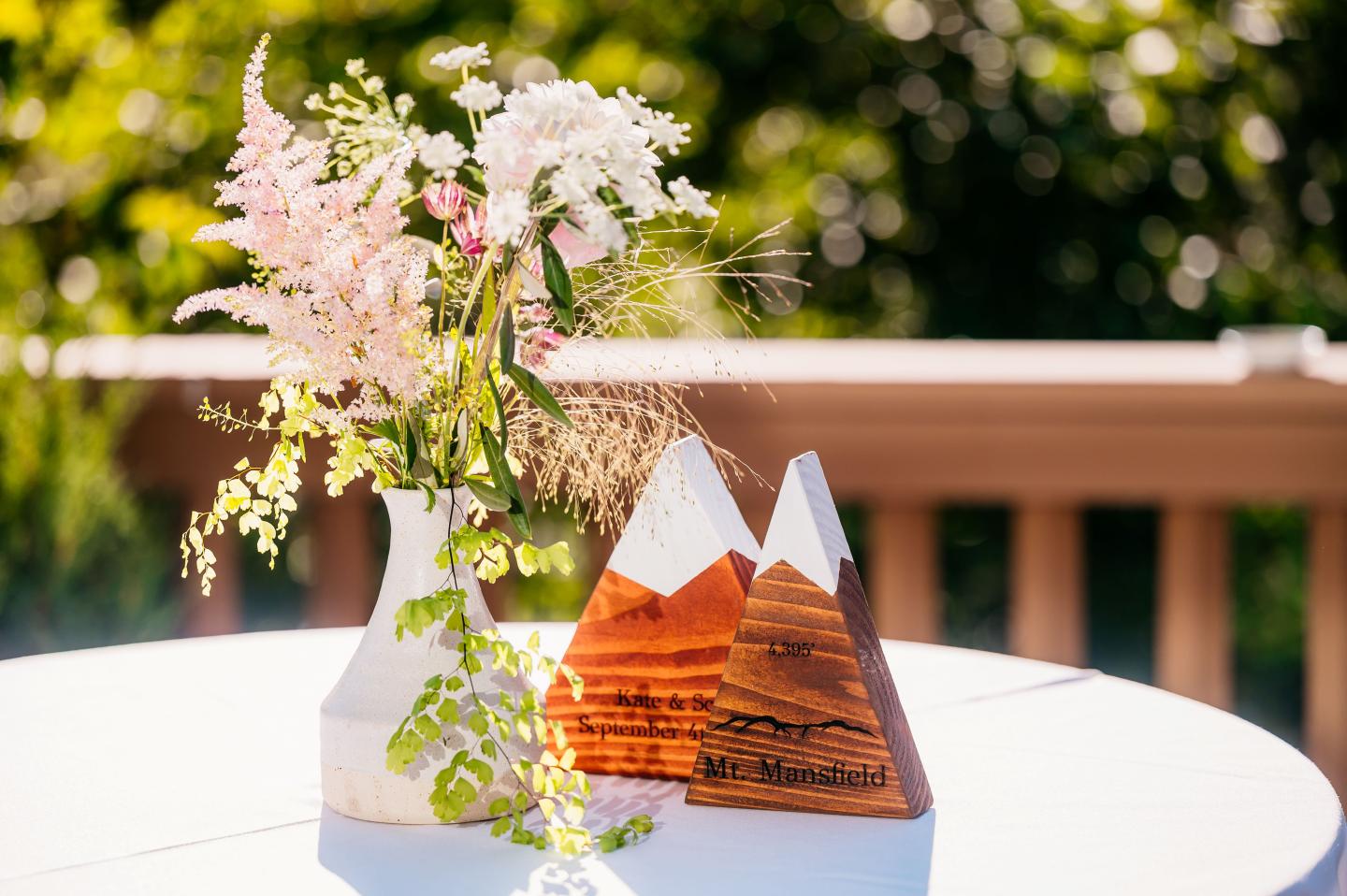 Vase with flowers next to wooden mountain decor on a sunlit table.