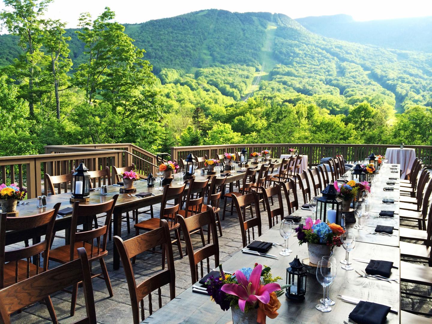 Outdoor tables with flowers set up on a deck overlooking lush green mountains.