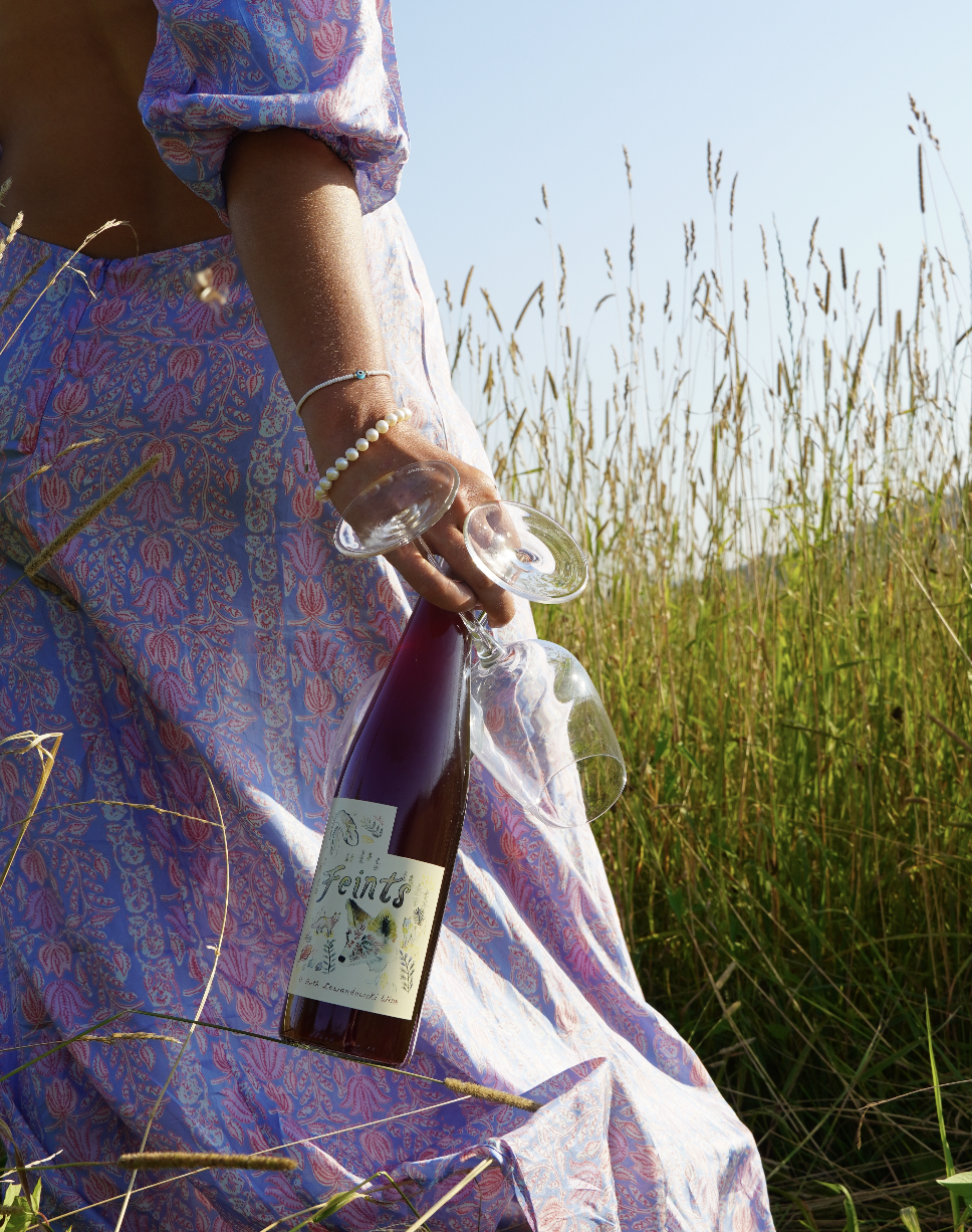 Woman in floral dress holding a wine bottle in a grassy field.