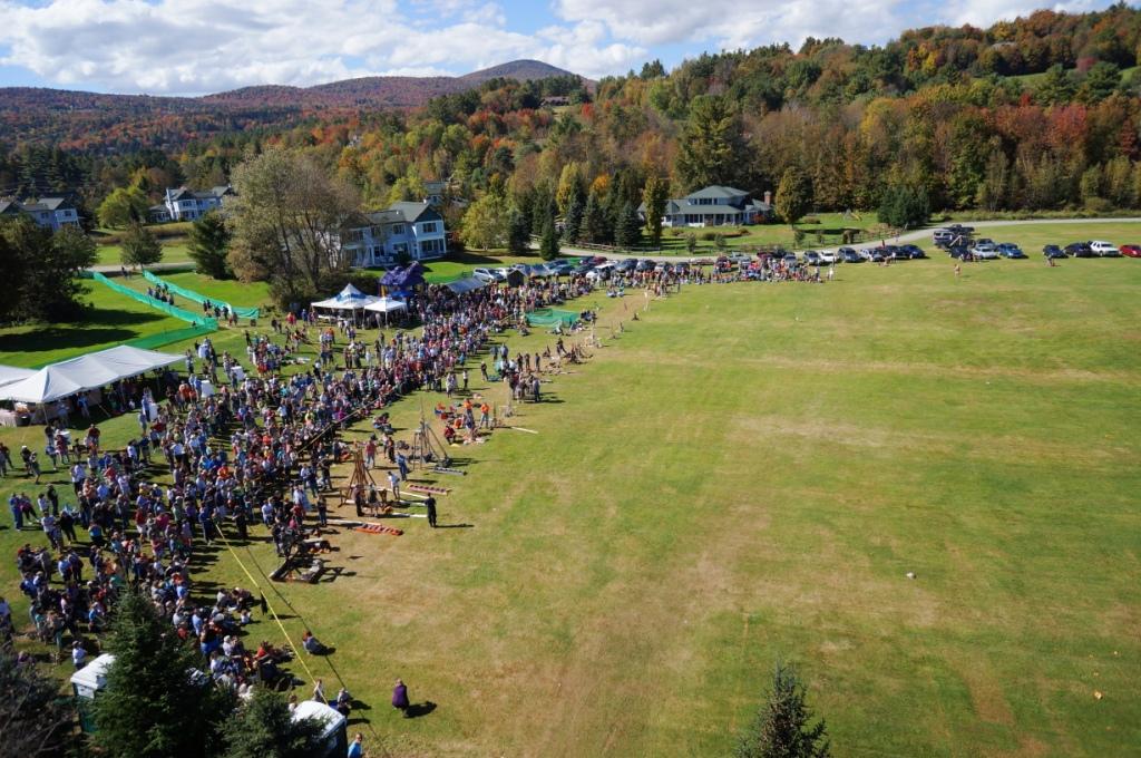 Crowd gathered on a grassy field surrounded by colorful autumn trees.