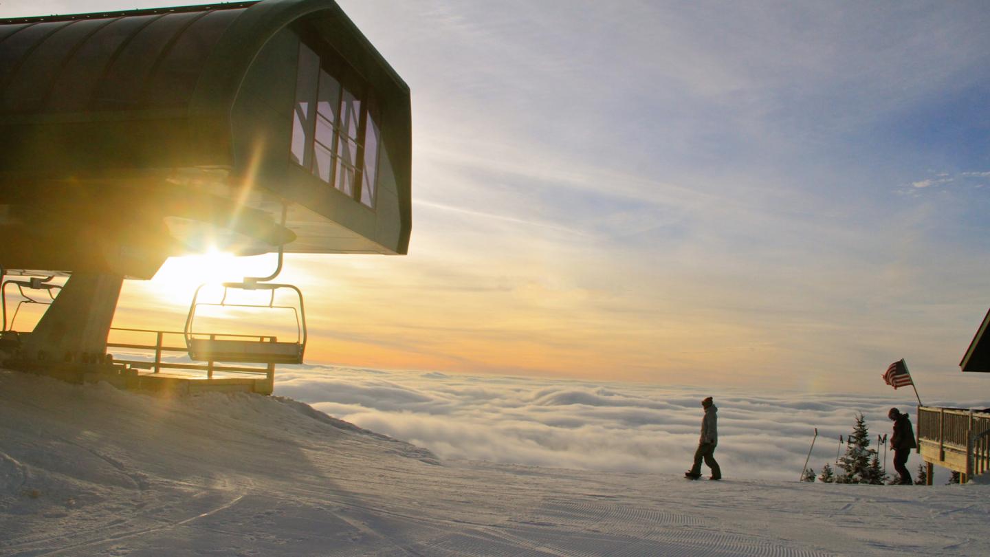 Ski lift at sunrise with people walking nearby, snowy landscape.