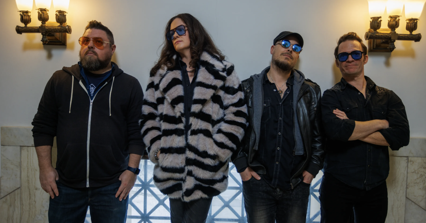 Group of four people in sunglasses, standing casually indoors.