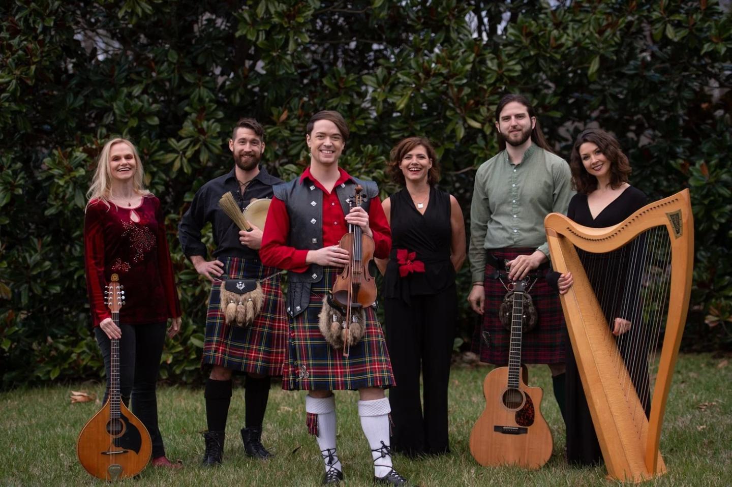 A group in traditional attire with instruments standing outdoors, smiling.