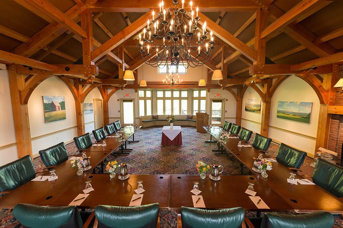 Spacious conference room with chandeliers, wooden beams, and a long U-shaped table.