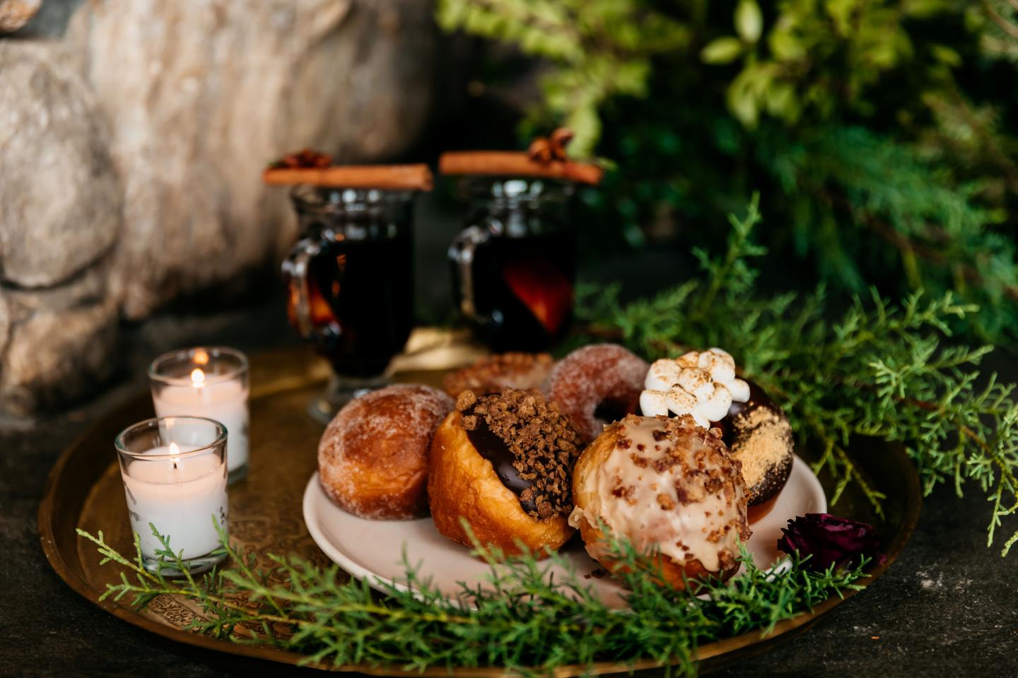 Donuts on a plate with candles, greenery, and mulled wine glasses nearby.