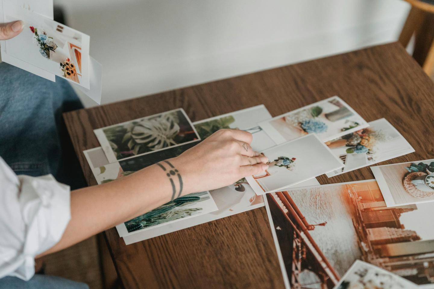 Person sorting photographs on a wooden table.