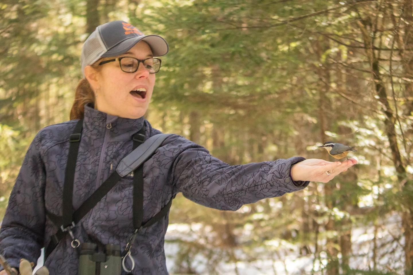 Woman in woods with a bird perched on her outstretched hand.