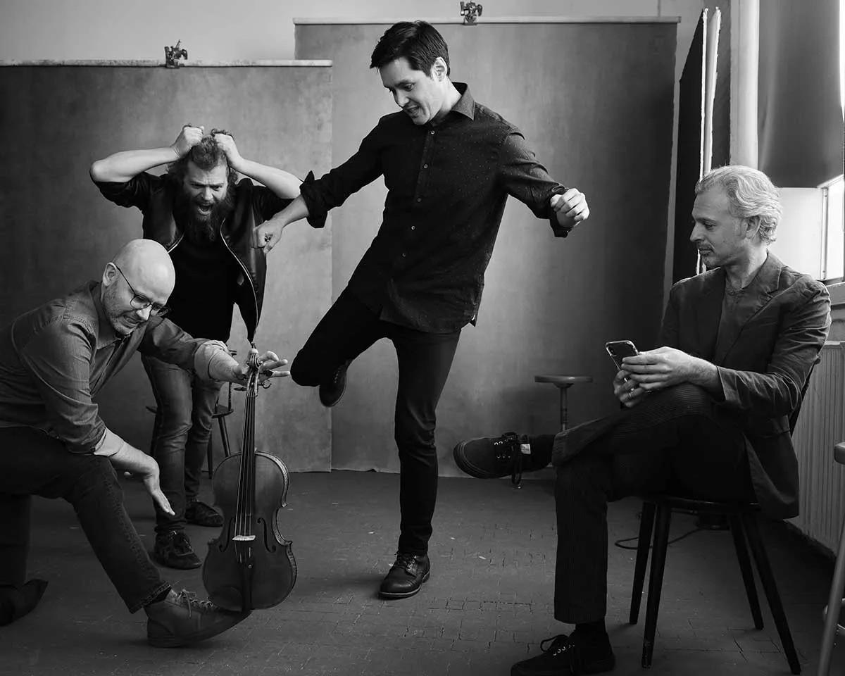 Four men in a playful pose with a cello, black and white photo.