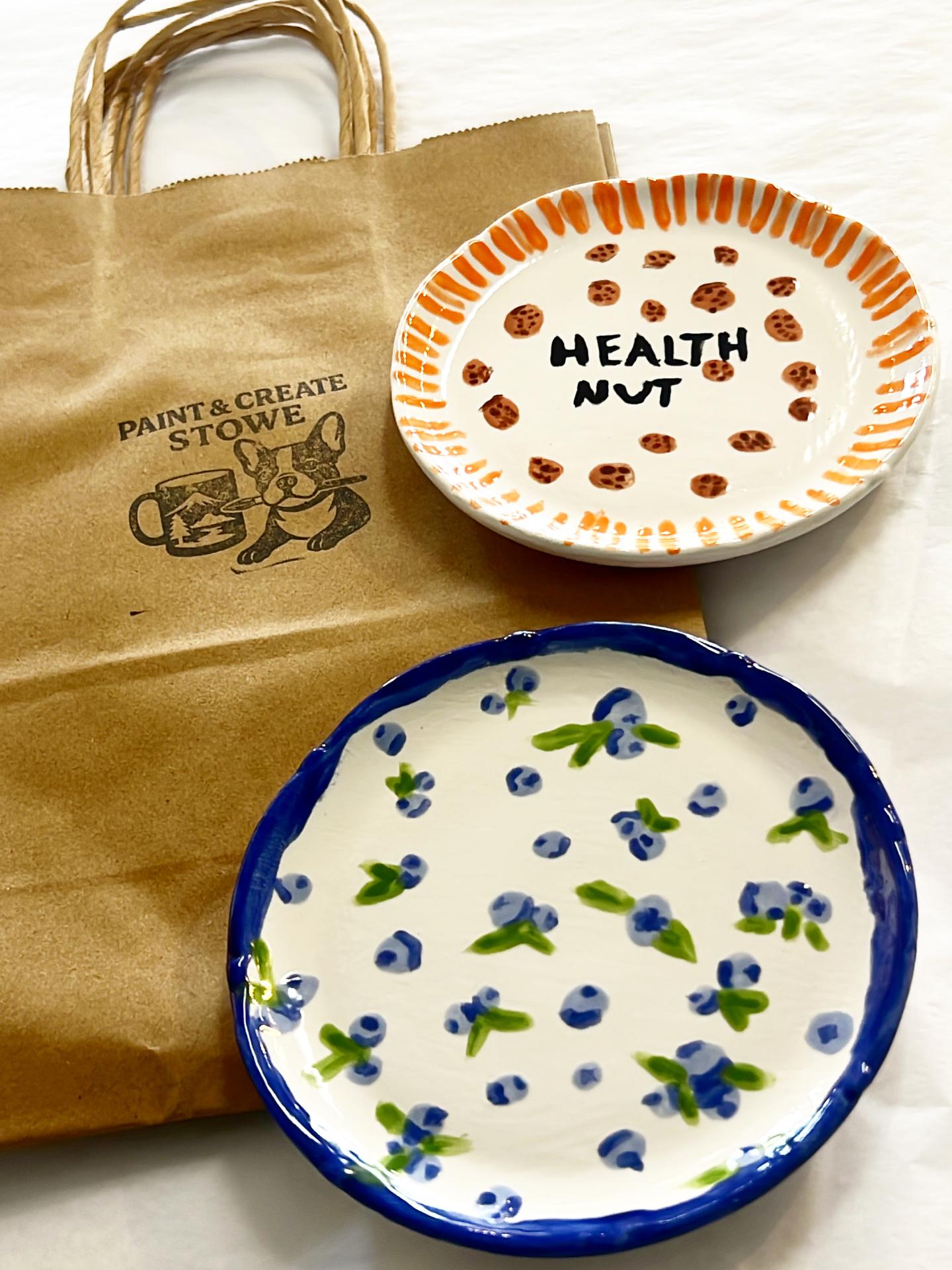 Brown paper bag with two decorative plates, one with orange dots, one with blue flowers.