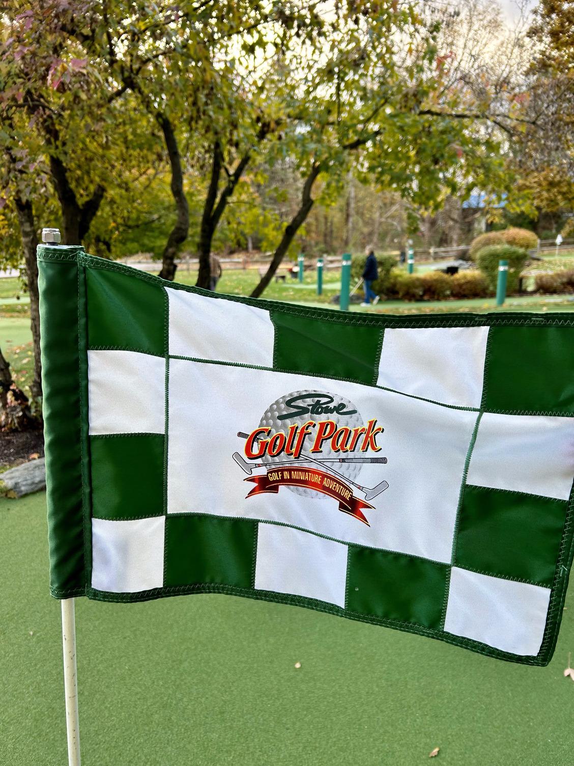Checkered flag on a golf course, trees and green grass in the background.