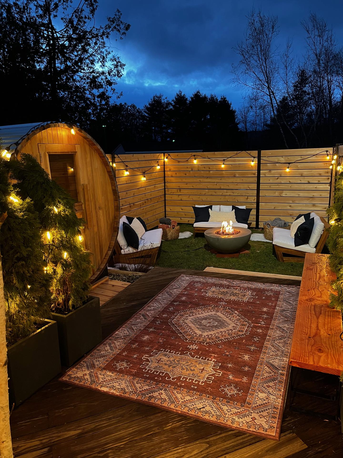 Cozy patio with string lights, outdoor seating, and a rug at dusk.