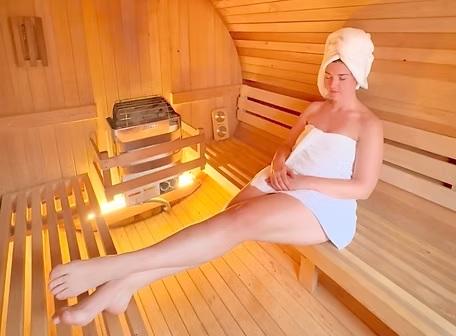 Woman relaxing in a sauna with a towel and head wrap, warm wooden interior.