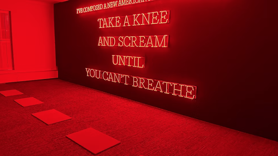 Red-lit room with neon words on a black wall, stepping stones on the floor.