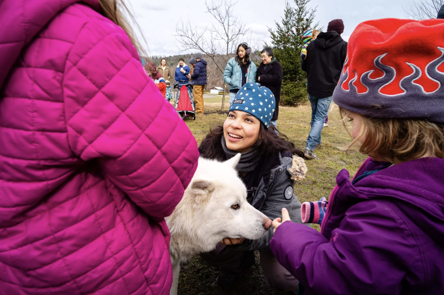 Woman and children petting a fluffy white sled dog outdoors.