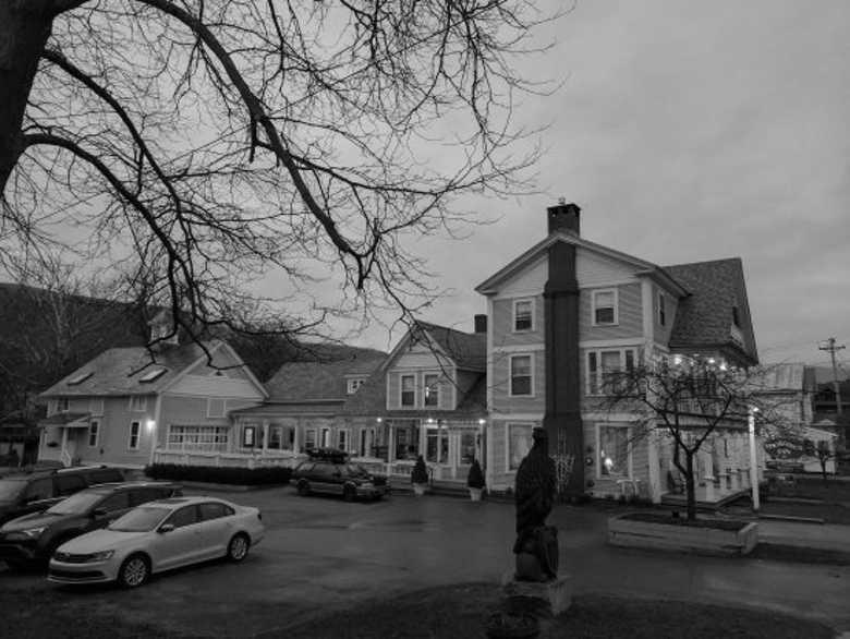 Grayscale photo of the old haunted stage coach inn under bare trees at dusk.