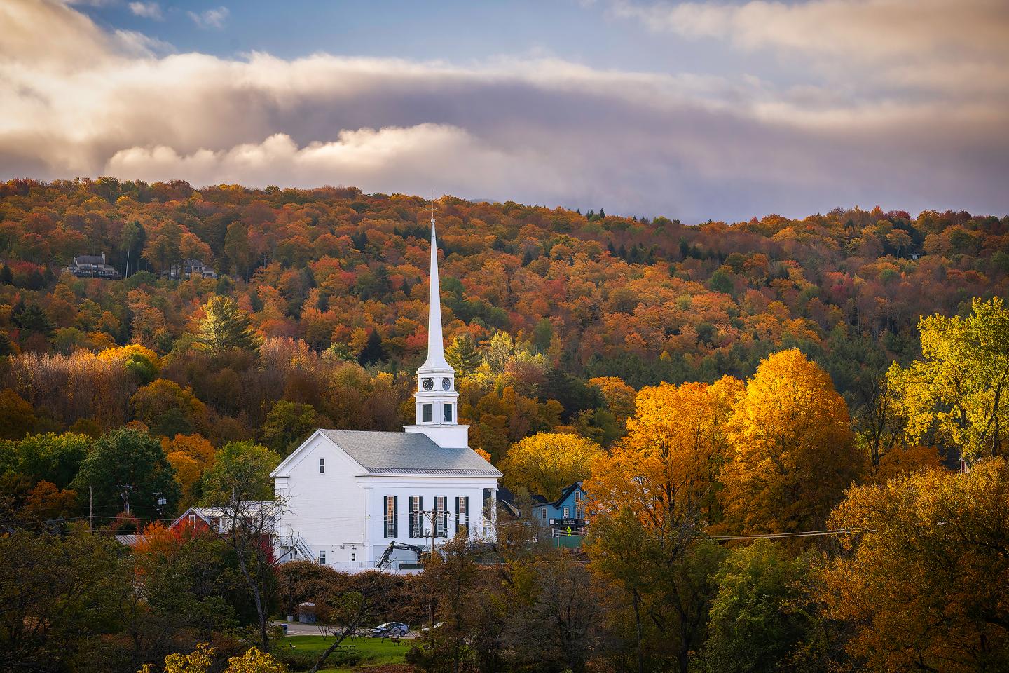White church with a tall steeple amidst vibrant autumn trees.
