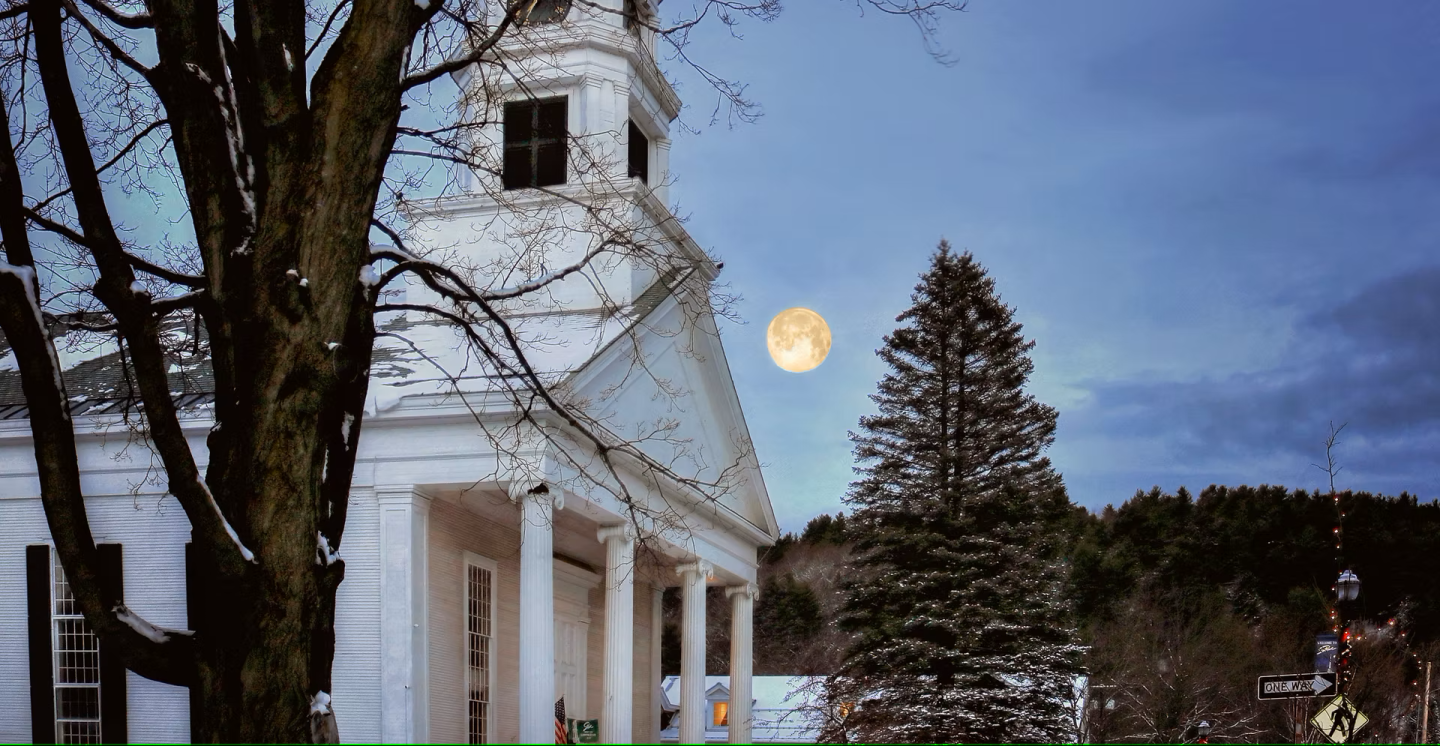 White church with a steeple, full moon, and tree at dusk.
