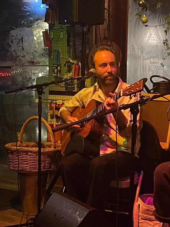 Musician playing guitar in a dimly lit cozy room.