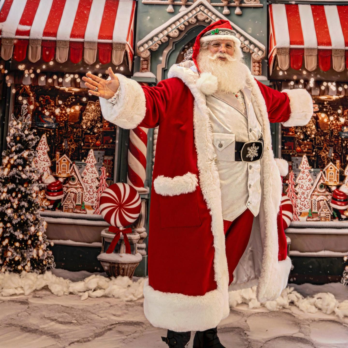 Santa Claus standing joyfully in front of a festive, snowy backdrop with candy decorations.