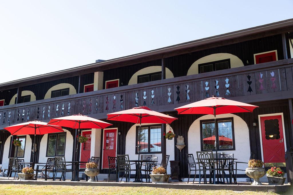Wooden lodge with red umbrellas and patio seating in front.