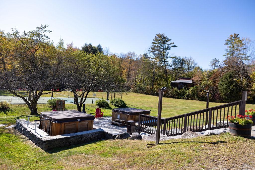 Two hot tubs on a patio, surrounded by trees under a clear blue sky.