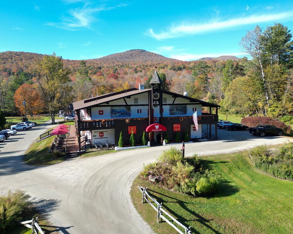 Chalet-style building with red umbrellas, set among autumn foliage and mountains.