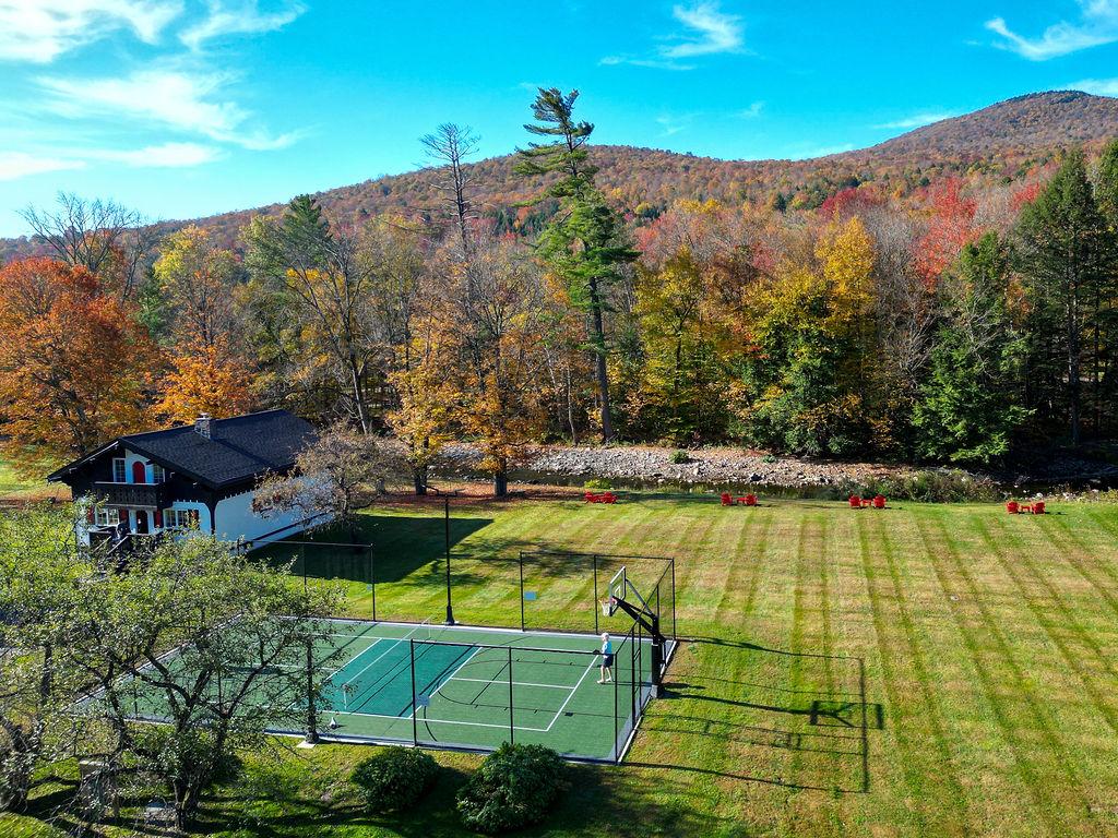 Aerial view of a house, tennis court, and autumn trees in a hilly landscape.