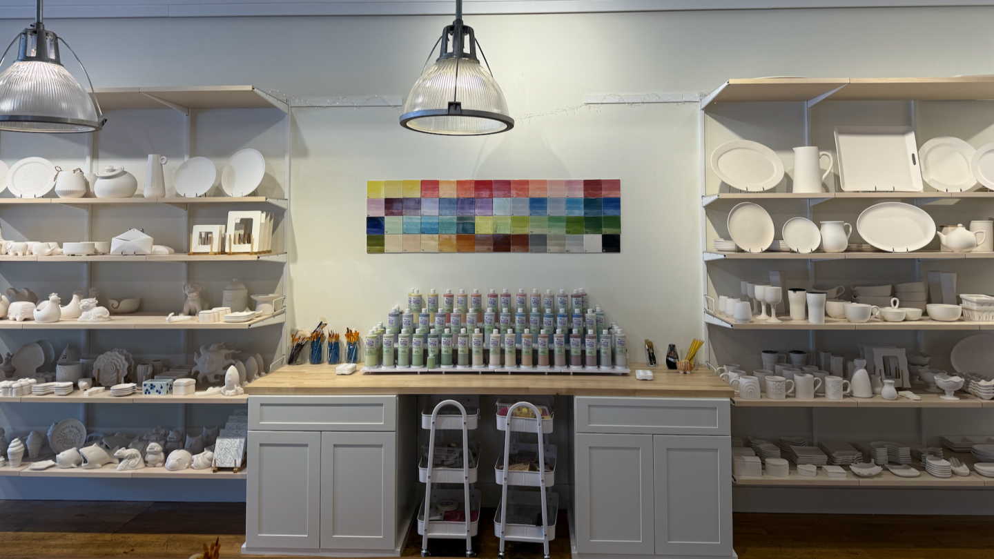 Pottery studio shelves with paint, pottery, and colorful palette chart.