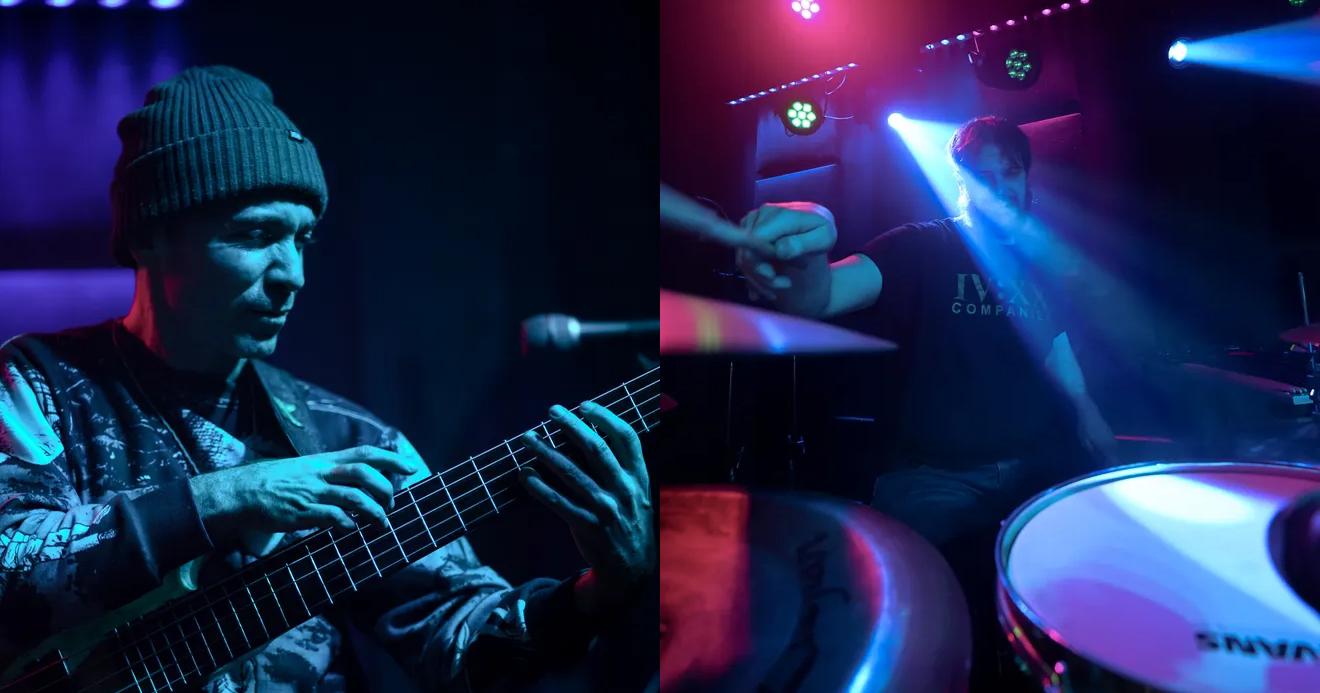 Musician playing guitar; drummer under blue and pink stage lights.