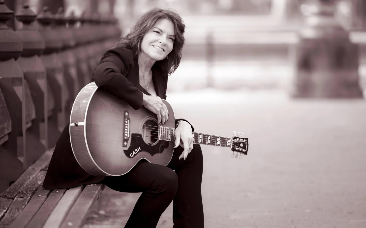Smiling woman with a guitar sits on a bench, sepia-toned photo.