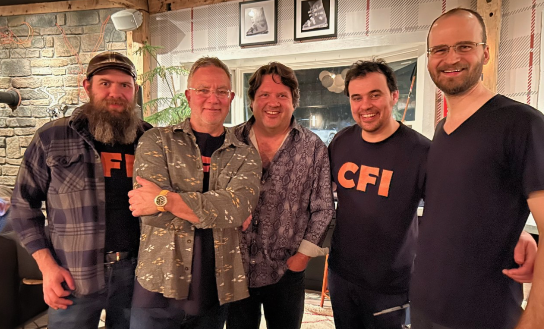 Group of five men smiling indoors, casual attire.