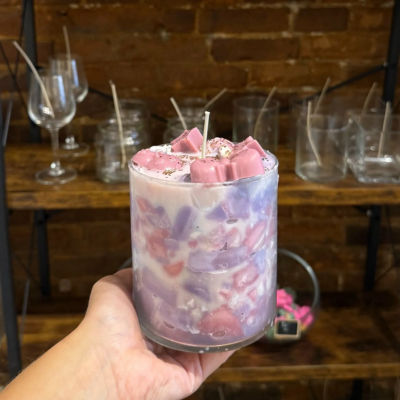 Hand holding a glass jar filled with colorful wax chunks and wicks.